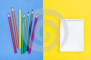 Colored pencils and a notepad on a two-color background