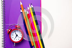 Colored pencils and purple notebooks and a red alarm clock. School and office supplies.