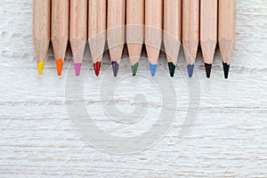 Row of colored pencils on white wooden background