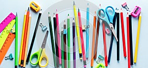 Colored pencils, scissors, notebook, ruler, pen, eraser, sharpener and more in glass. School and office stationery on light blue