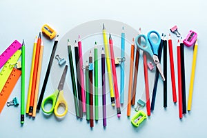 Colored pencils, scissors, notebook, ruler, pen, eraser, sharpener and more in glass. School and office stationery on light blue b