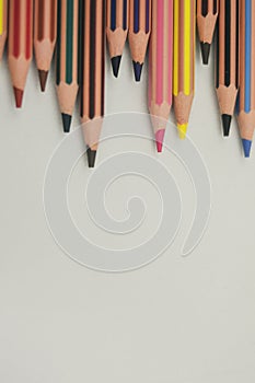 Colored pencils from the top margin, well sharpened, on white background, unaligned and vertical perspective