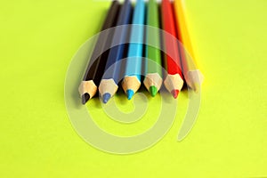 Colored pencils on a yellow background. 6 colors: Black, blue, blue, green, red, yellow. Pencils are well-honed. Flatlay. Isolated