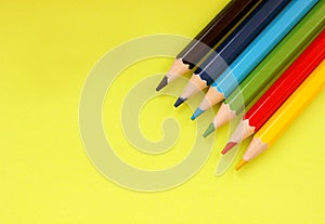 Colored pencils on yellow background. 6 colors Black, blue, blue, green, red, yellow. Pencils are well-honed. Flatlay. Isolated.