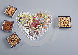 Colored pills in the shape of a heart and different types of nuts on a gray background. Traditional medicine and healthy