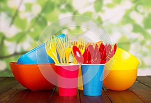Colored plastic tableware: bowls, forks, spoons on abstract green .