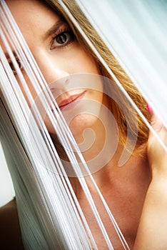 Colored portrait of a young attractive woman, slanted, which is partially obscured by the white threads of a string curtain.