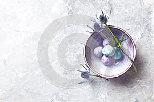 Colored quail eggs and sea holly flowers in a ceramic bowl flat lay arrangement