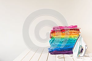 Colored rainbow clothes are stacked on the table. The iron stand