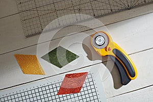 Colored rhombuses, rotary cutter, ruler and cutting mat on a white wooden surface