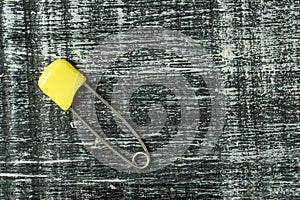 Colored safety pins. yellow safety pin on black and white wood background