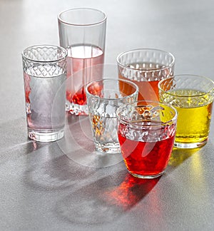 Colored soft drinks in glass faceted glasses on a gray table. Photo with a gradient background