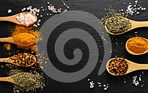 Colored spices on wooden spoon on slate dark background with copy space