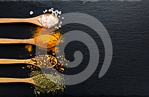 Colored spices on wooden spoon on slate dark background with copy space