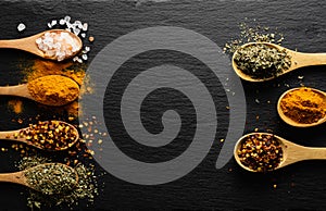 Colored spices on wooden spoon on slate dark background with copy space