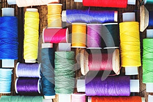 Colored spools of thread laid out in rows on wooden background
