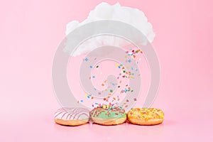 Colored sprinkles fall from cloud. Assorted donuts frosted, pink glazed and sprinkles on pink background