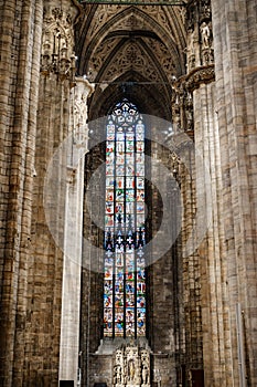 Colored stained glass window against the columns and arched ceiling in the Duomo. Italy, Milan