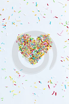 Colored sugar sprinkles are collected in the shape of a heart isolated on a white background
