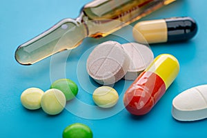 Colored tablets, capsules and injections for treatment. Blue background, studio shot.