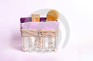 Colored terry bath towels, soap and a dry massage brush in a basket on a white background