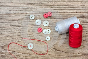 Colored thread coils and Button and needle on wood background with text space.
