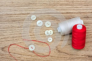 Colored thread coils and Button and needle on wood background with text space.