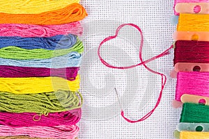 Colored thread for embroidery on white canvas, a needle with red thread in the shape of a heart. The concept of love for a hobby.