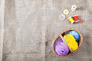 Colored threads and wooden buttons and a wicker basket are on sackcloth in the corner of the frame