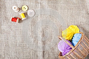 Colored threads and wooden buttons and a wicker basket are on sackcloth in the corner of the frame