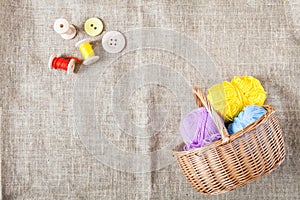 Colored threads and wooden buttons and a wicker basket are on sackcloth in the corner of the frame