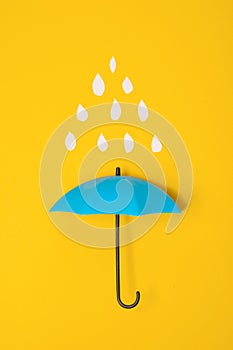 Colored umbrellas on a yellow background and paper raindrops. Conceptuality and place for the text