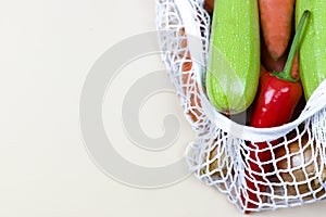 Colored vegetables in a koton string shopping bag on a neutral beige background. eco zero waste concept. no plastic