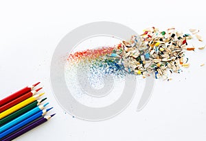 Colored watercolor pencils of rainbow colors and shavings from them after sharpening on a white background.