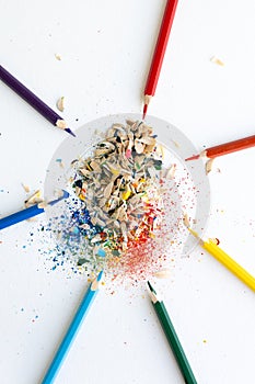 Colored watercolor pencils of rainbow colors and shavings from them after sharpening on a white background