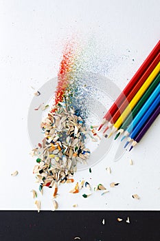 Colored watercolor pencils of rainbow colors and shavings from them after sharpening on a white background.