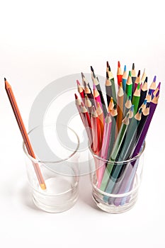 Colored wood pencils in front of simple graphite pencil on table in glasses isolated