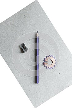 A colored wooden pencil sharpen with a sharpener and shavings lie on a white and gray background