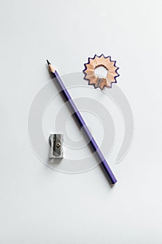 A colored wooden pencil sharpen with a sharpener and shavings lie on a white and gray background