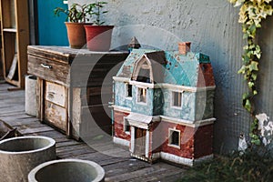 Colorful abandoned dollhouse next to an old wooden bedside table with potted plants in yard