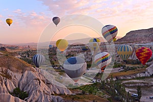 Colorful air balloons fly up into the sky at sunrise among a beautiful rocky landscape. C