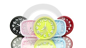 Colorful alarms ticking show different times, reflecting in glass table