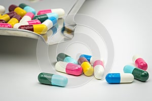 Colorful of antibiotic capsules pills on stainless steel drug tray and some of them on white background