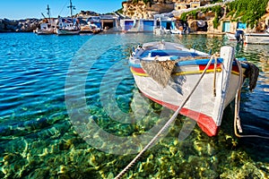 Colorful authentic Greek fishing boat anchored in small village in crystal clear waters. Whitewashed boat garages, blue