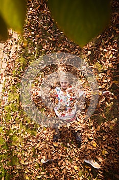 Colorful autumn and happy child lying in orange, yellow leaves