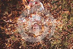 Colorful autumn and happy child lying in orange, yellow leaves