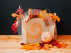 Colorful autumn leaves in paper bags and piggy bank near. Sale and shopping concept