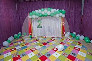 Colorful baby carpet. White and green balloons. Pink curtain.Two inscriptions with green artificial flowers. 2 Age decor