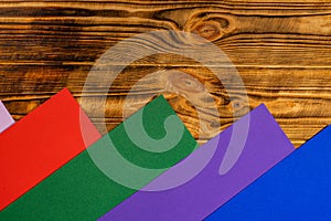 Colorful background with rainbow colored stripes and brown wooden texture. Red, green, purple and blue stripes of paper