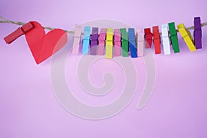 Colorful background of a red heart and wooden paper clips on rope on soft pink purple background. Copy space. Backgrounds for photo